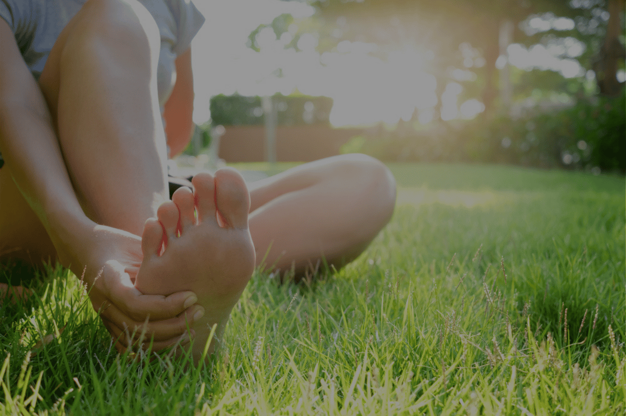 Barefoot woman sitting on the green grass thinking about athletes foot infection