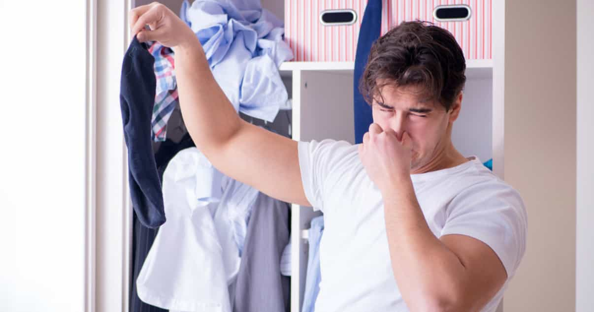 Man smelling his sweaty clothes before washing them to avoid a fungal infection