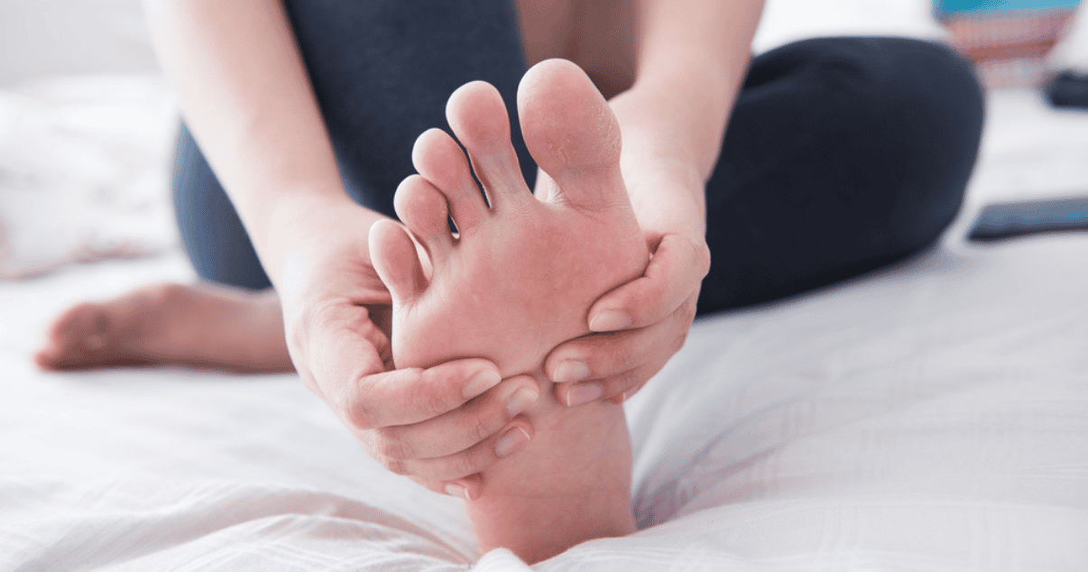 Woman touching her foot sitting on the floor worried about athletes foot symptoms